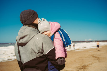 Father and pretty little daughter walking along snowy beach of finland gulf. Image with selective...