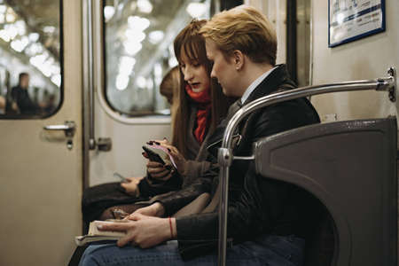 young caucasian women sitting in subway carriage looking at smartphone. Image with selective focus, toning and noise effectの写真素材