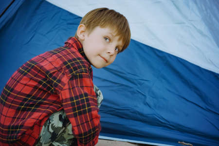 cute little caucasian boy sitting on sand barefoot by touristic tent. Family camping concept. high quality photoの写真素材