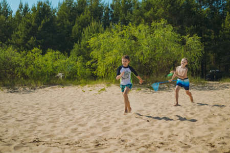cute caucasian boys running along sand beach into water with laughter. vacation on the seaside. happy childhood. Trees and bushes on backgroundの写真素材