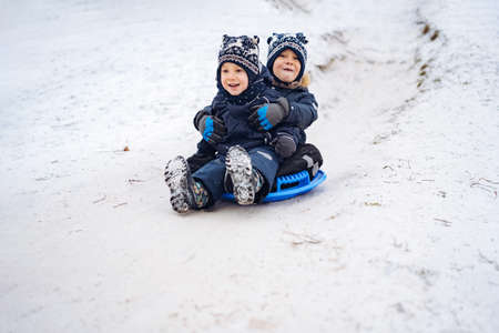 cute caucasian boys sliding down the icy slope in park . Winter activities concept. happy childhood. Image with selective focus. high quality photoの写真素材