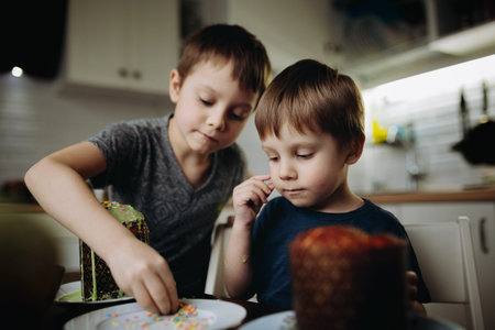 Brothers decorating Easter cakes with glace icing eating sugar topping. Image with selective focus.