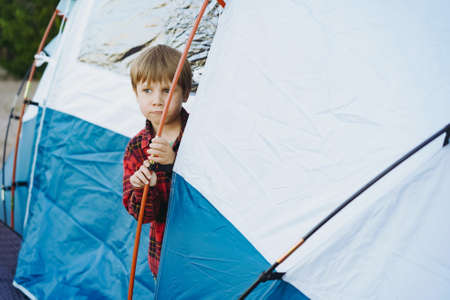 cute little caucasian boy looking out from touristic tent. Family camping concept. high quality photoの写真素材