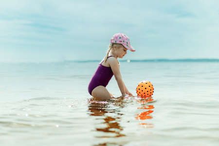 cute little girl playing with rubber ball in sea. Summer beach vacation concept.の写真素材