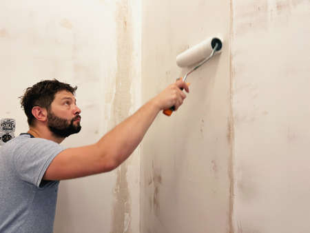 home improvement. Caucaisan man applying wall treatment, putting up glue for wallpaper using construction rollerの写真素材