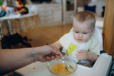 mother feeding baby daughter sitting in high chair at home. high quality photoの写真素材