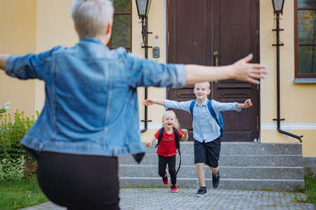 Mother meets children from school. Caucasian boy and girl running towards mom opening arms to catch. Back to school conceptの写真素材