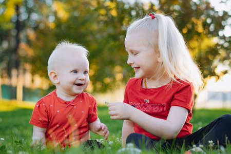 little sisters together in the park. Caucasian blonde girl giving flower to her adorable baby sister.の写真素材