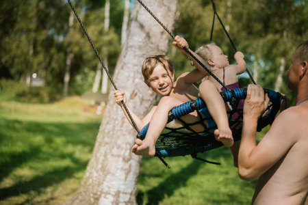 Father pushing little son sitting on swing at playground. Summer in nature. Quality time with family on vacationの写真素材