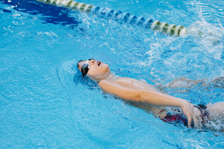 little caucasian boy wearing goggles swimming backstroke style in a pool. Image with selective focus