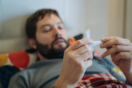 caucasian man staying in bed measuring temperature feeling sick