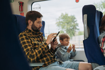father and child travelling by train. Man using smartphone, boy eating appleの写真素材