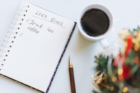 open notepad with text new year resolutions. and empty list. Flower, laptop and smartphone on...