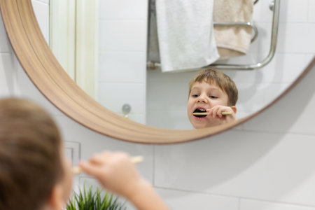 cute 5 years old boy brushing teeth with bamboo tooth brush in bathroom looking at himself in mirror. Image with selective focus. high quality photoの写真素材