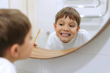 cute 8 years old boy washing face in bathroom looking in mirror and smiling. Image with selective focus.の写真素材