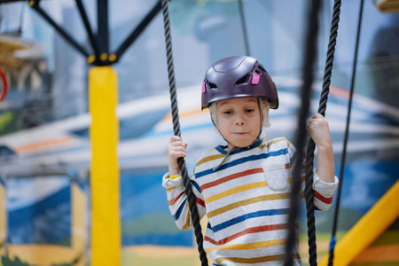 caucasian boy of 8 years old climbing in adventure park passing obstacle course. high rope park indoors. high quality photoの写真素材