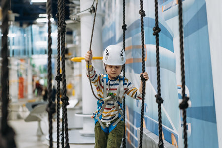 caucasian boy of 8 years old climbing in adventure park passing obstacle course. high rope park indoors. high quality photoの写真素材