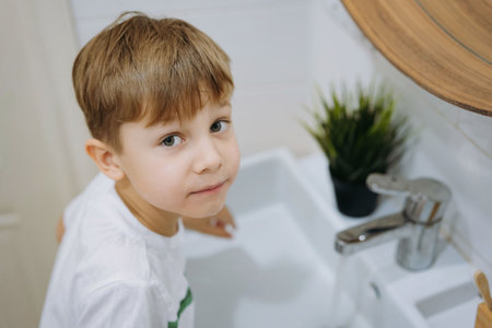 cute 5 years old caucasian boy going to wash his face and brush teeth with bamboo brush over the sink in bathroom. Image with selective focusの写真素材