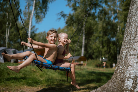 cute little boy and girl having fun on a spiderweb tree swing at playground. Summer vacation in the nature.の写真素材