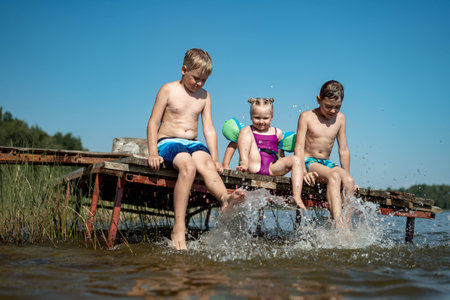 Three children playing on the pier in the water on a sunny dayの写真素材