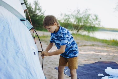 cute little caucasian boy helping to put up a tent. sunset shadows from trees. Family camping concept. high quality photoの写真素材