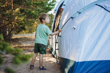 cute little caucasian boy helping to put up a tent. sunset shadows from trees. Family camping...