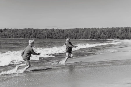 cute caucasian boys wearing red hoodies and blue underpants running from waves in Ladoga lake with enthusiasm. Image with selective focus. high quality photoの写真素材