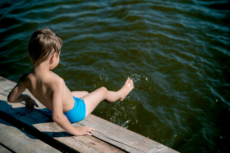 cute caucasian boy sitting on wooden pier diving into lake in countrysideの写真素材