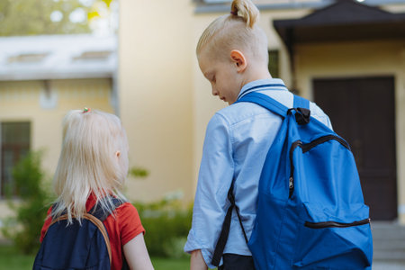 children walking to school with backpacks on sunny day having fun jumping kicking each other. Beginning of academic year. Boys by school doorstep. Image with selective focusの写真素材