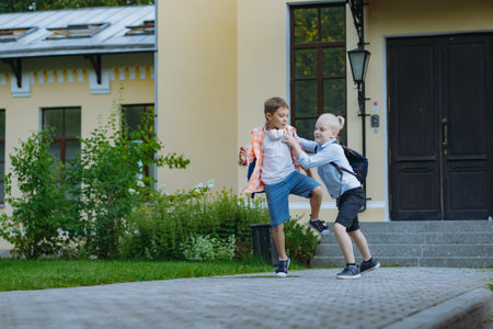 children running to school with backpacks on sunny day having fun jumping kicking each other. Beginning of academic year. Boys by school doorstep. Image with selective focusの写真素材