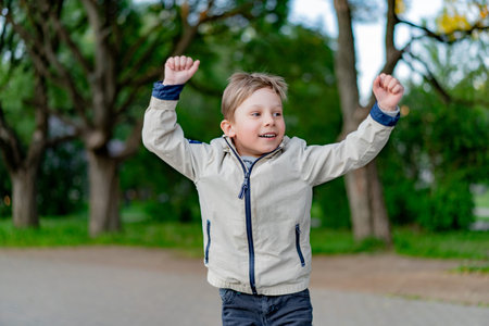 happy little caucasian boy triumphant with raised hands in parkの写真素材