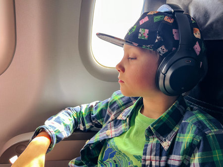 caucasian boy traveling by plane listening to music in headphones looking outside at aerial sky...