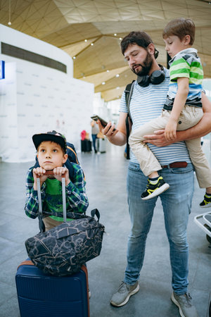Father holding cute caucasian boy in airport. Child with suitcase and backpack waiting for delayed flight. Traveling with kidsの写真素材