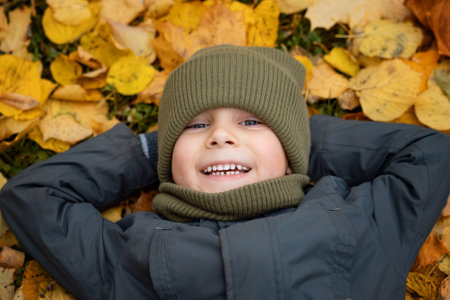 cute little boy laying on ground covered with yellow fallen leaves. high quality photoの写真素材