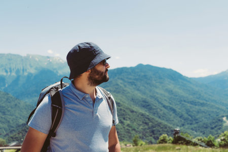 millenial bearded tourist man wearing bucket hat, with backpack trekking in mountainsの写真素材
