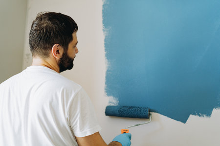 caucasian bearded man painting wall with paint roller. Painting apartment, renovating homeの写真素材