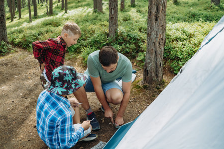 caucasian man putting up a tent in pine forest. children helping him. Family camping conceptの写真素材