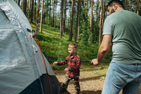 caucasian man putting up a tent in pine forest. Boy is helping him. Family camping concept
