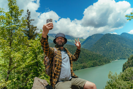 Hiking traveller handsome caucasian bearded man with backpack taking selfie against view of Lake Ritsa in Abkhaziaの写真素材