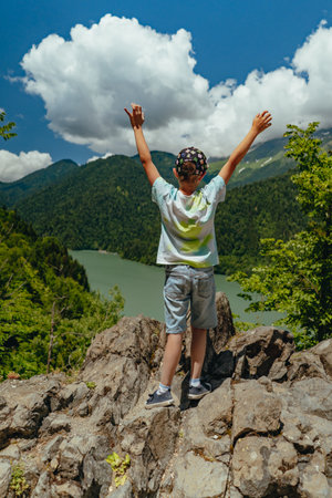 Hiking traveller caucasian boy with hands up enjoying beautiful view of turquois blue Lakeの写真素材