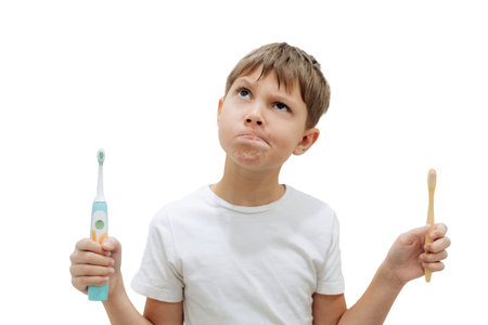cute 8 years old boy holding bamboo and electric tooth brush making choiceの写真素材