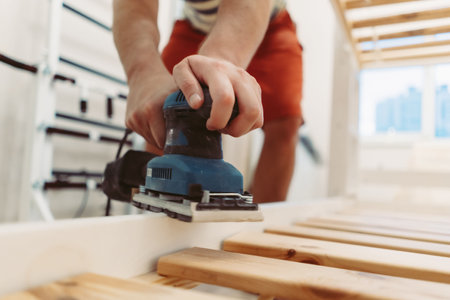 unrecognizable man rubs wooden child bed with power sander or grinder removing old paintの写真素材