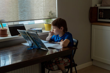 stressed tired boy doing homework at home at the desk by the window.