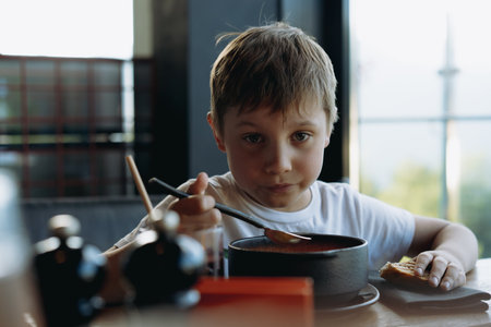 cute little boy eating soup with egg from bowl in restaurant. High quality photoの写真素材