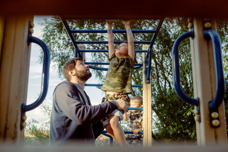 a boy doing chin-ups on monkey bars and father is helping him. Exercises on the playground on the beach. fathers day conceptの写真素材