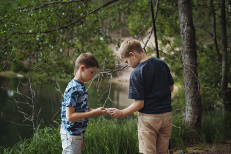 boys fishing by the lake in forest trying to untwine knot of fish wireの写真素材