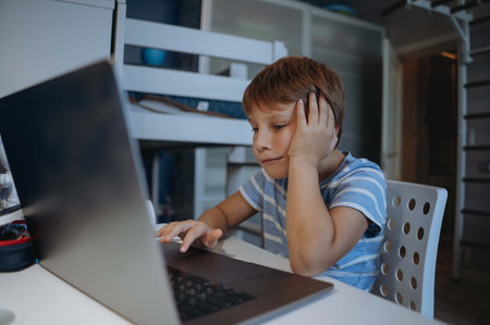 caucasian cute little boy studying at home usung laptop, tired, stressed, thinking hard trying to do homework. Distant learning, online lessonの写真素材