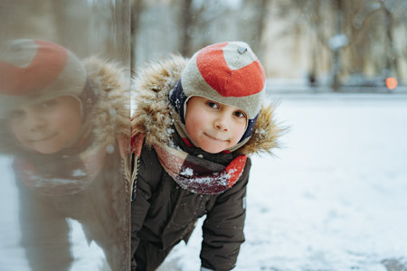 winter portrait of cute smiling caucasian boy of elementary age in knit hat with pompom in city. Image with selective focusの写真素材