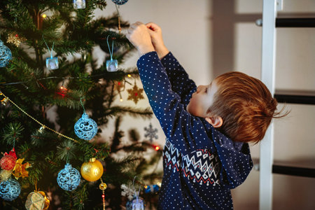 Little cute caucasian boy decorating Christmas tree with twinkling decorations. Image with selective focus.の写真素材