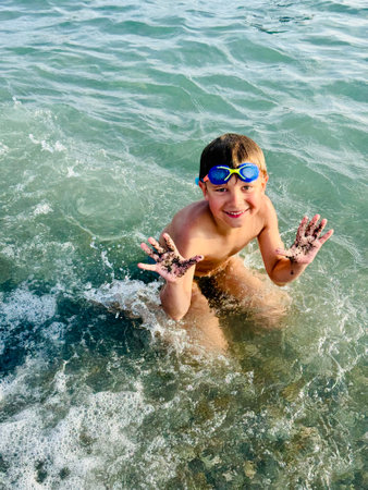 little boy wearing goggles splashing in sea waves happily laughingの写真素材